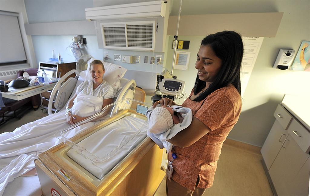 Woman in a hospital bed after giving birth, smiling at her doctor holding her newborn baby at Stevenson Memorial Hospital. 